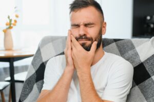 Emergency and Urgent Dental Pain - Man holding jaw with painful look